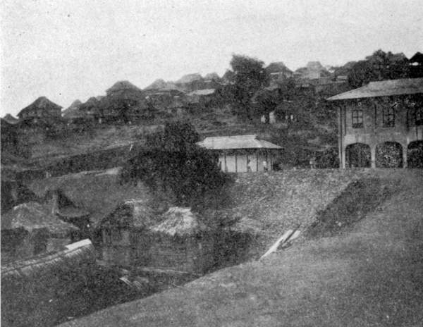 CONCRETE DORMITORY AND NATIVE SHACKS.